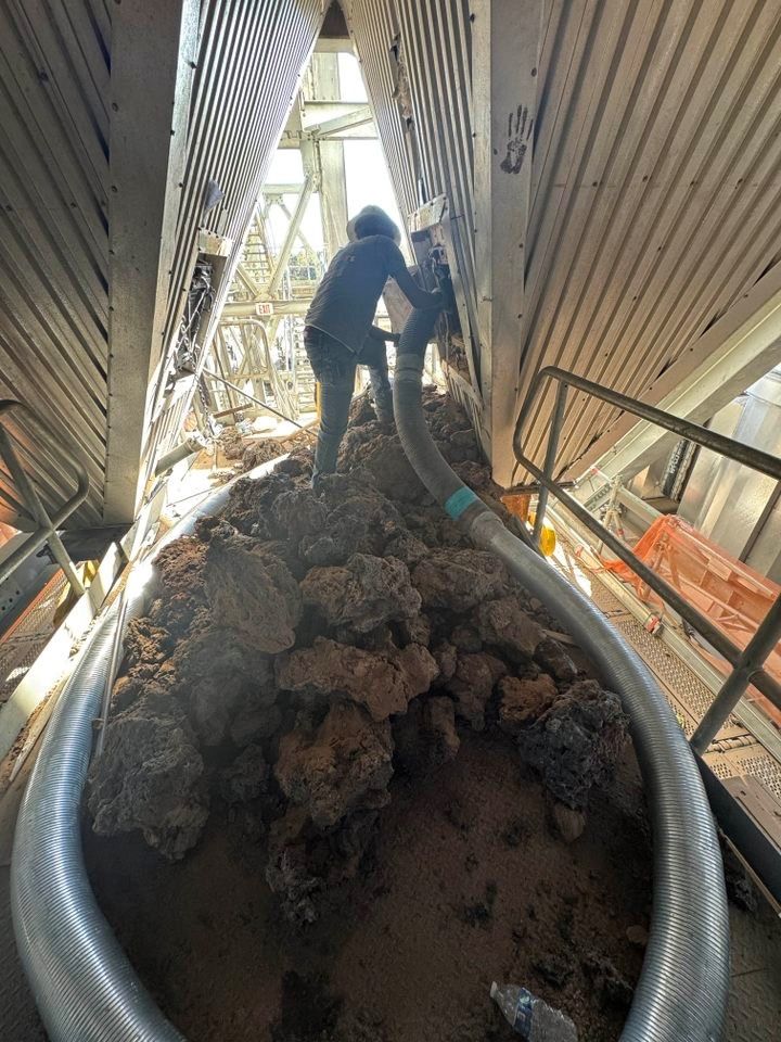 Person vacuuming debris inside a large industrial structure, with metal beams and pipes visible.