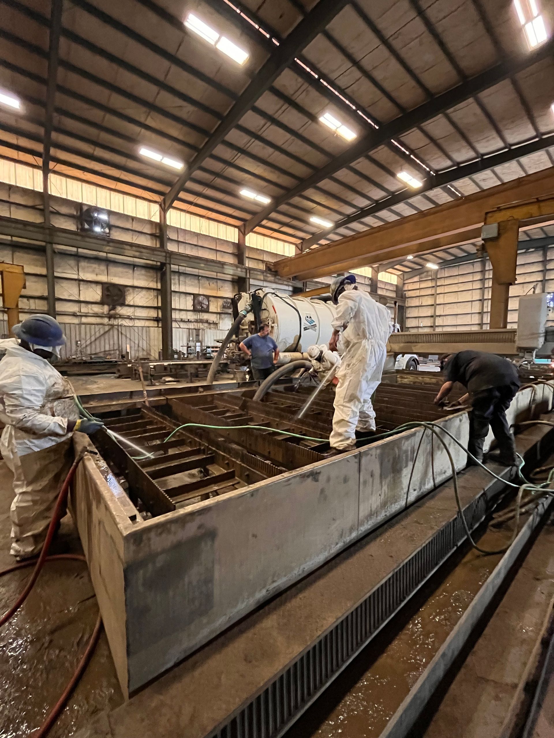 First Environmental employees are working on a large piece of metal in a factory.