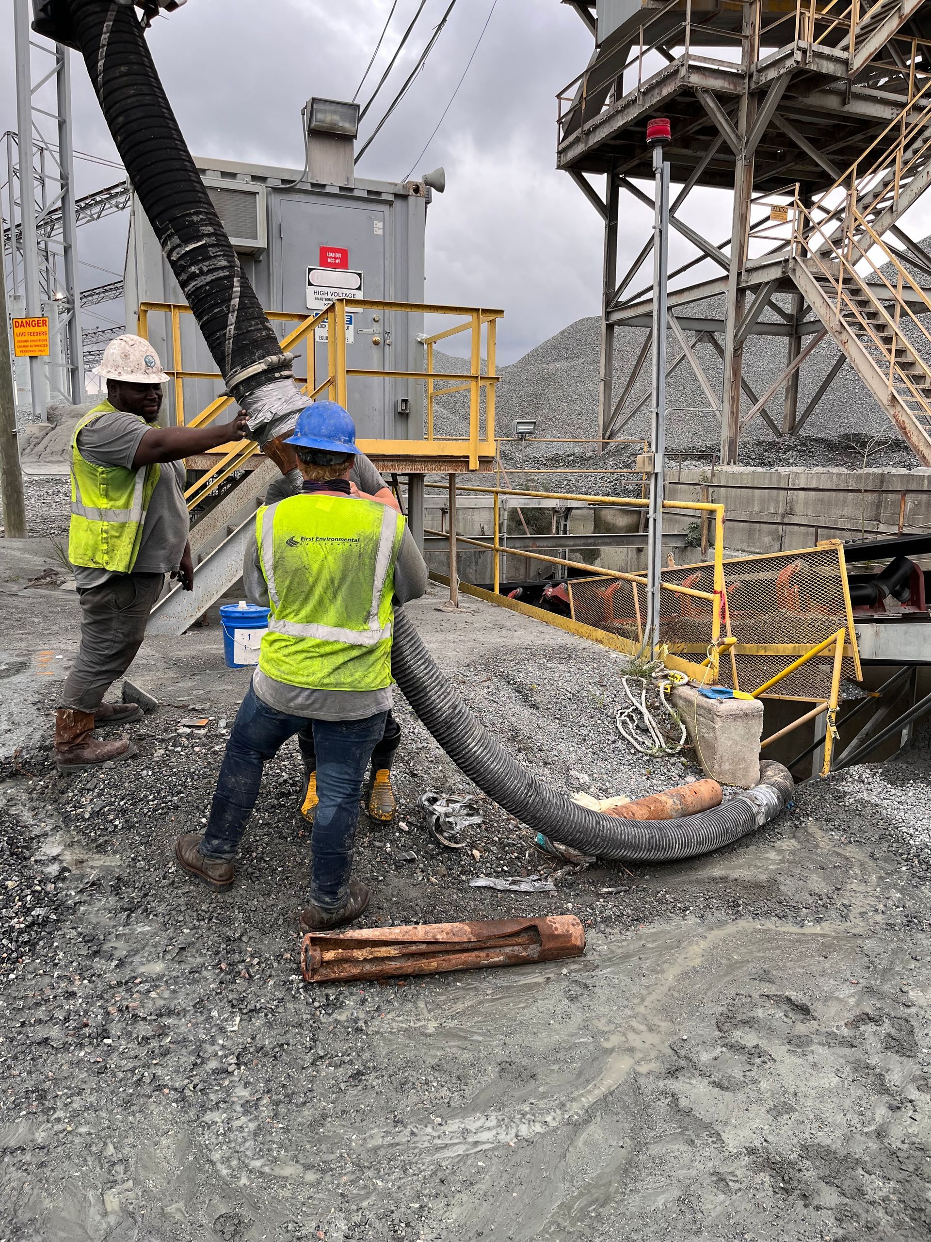 Two First Environmental workers are working on a large pipe in a gravel area.