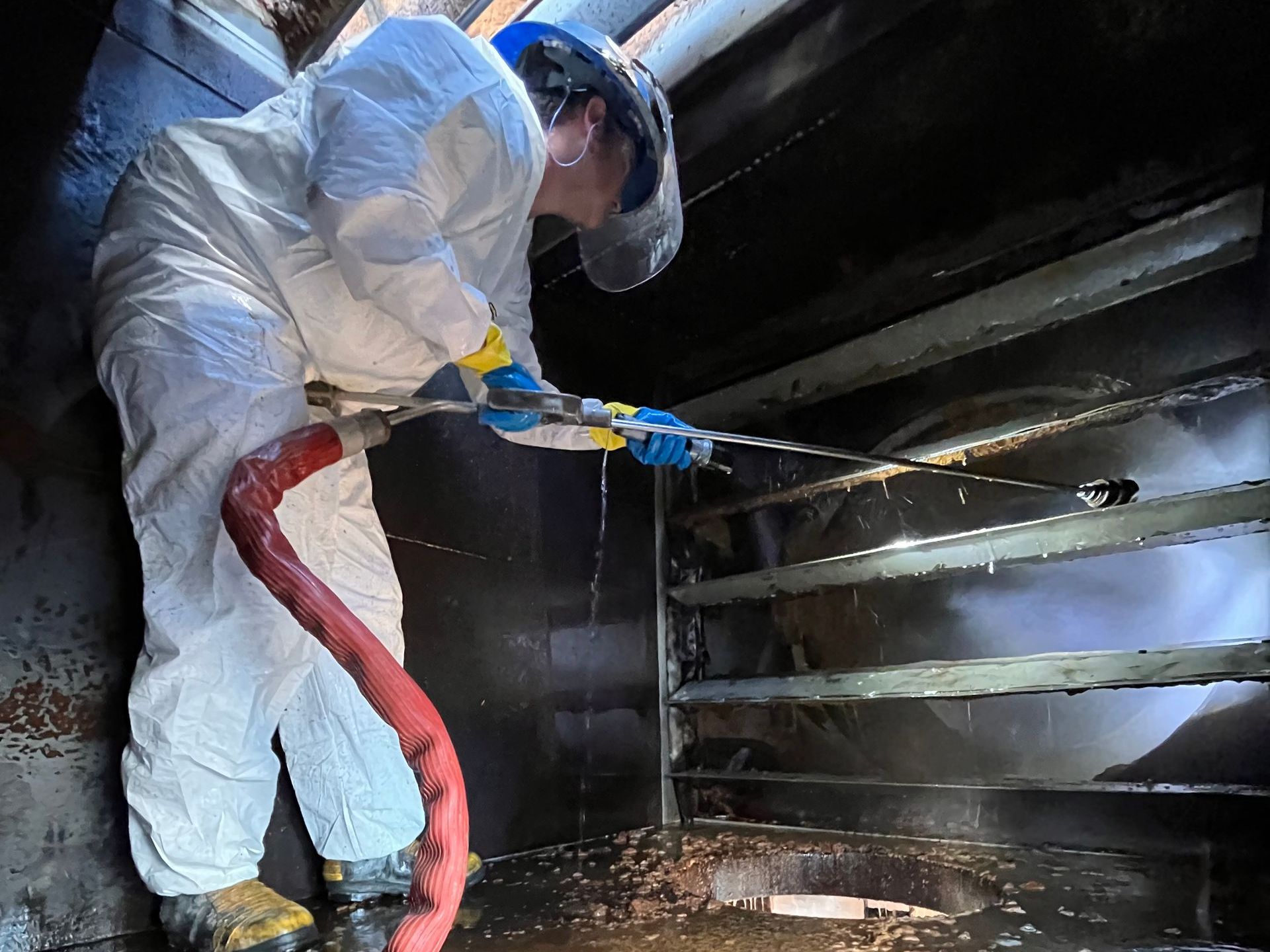 A man in a protective suit is cleaning a tank with a hose.