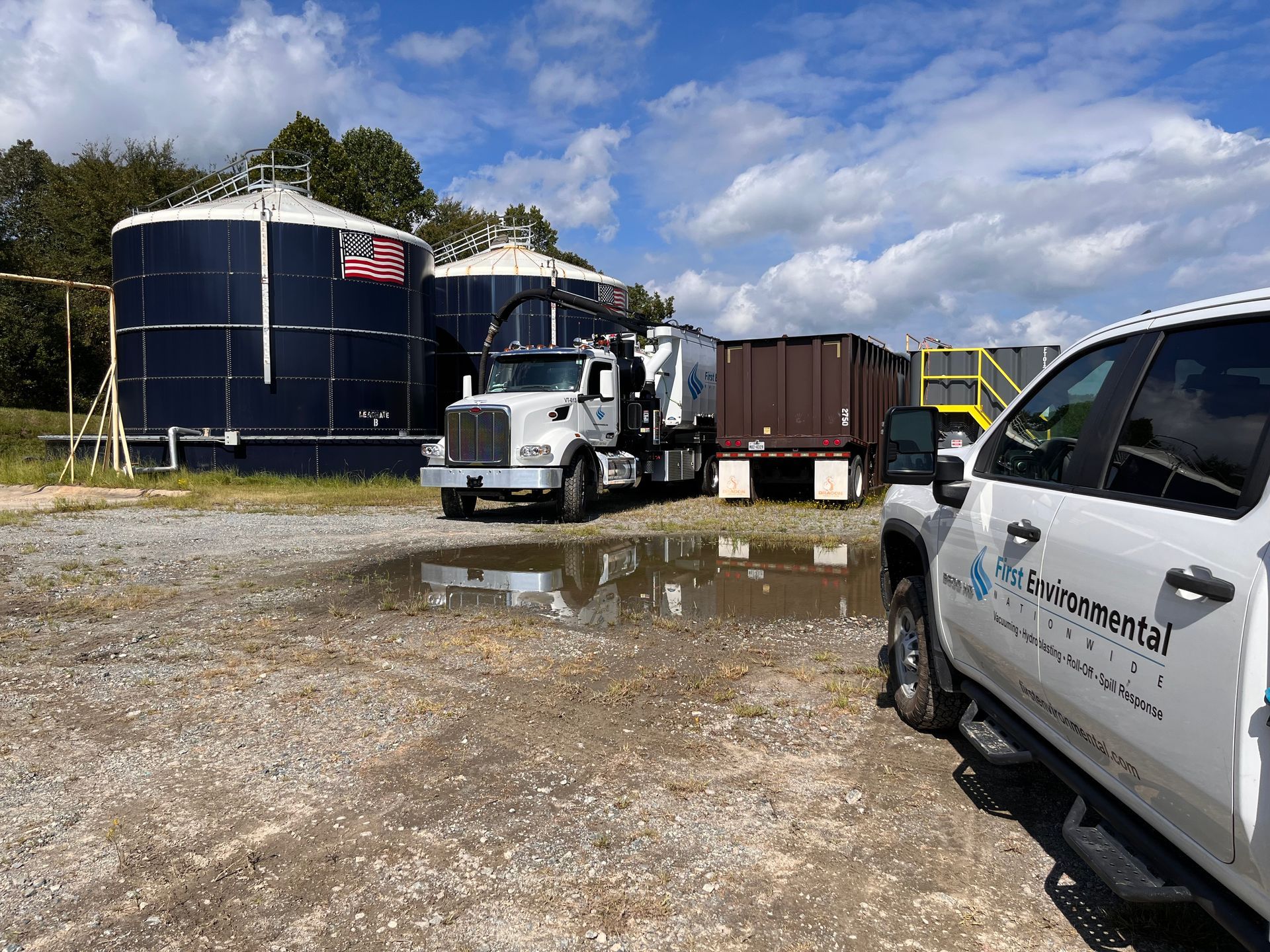 A white First Environmental truck is parked in front of a large tank.