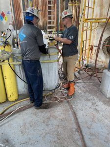 Two men are working on a tank in a factory.