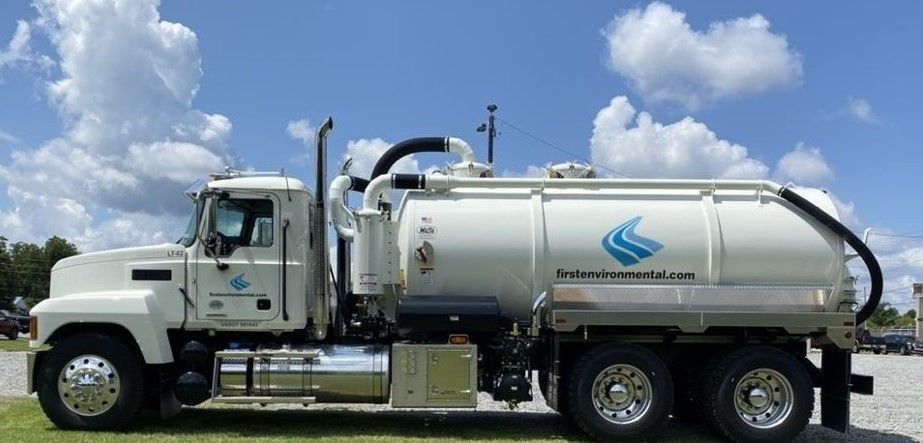 A white liquid vacuum truck is parked in a gravel lot.