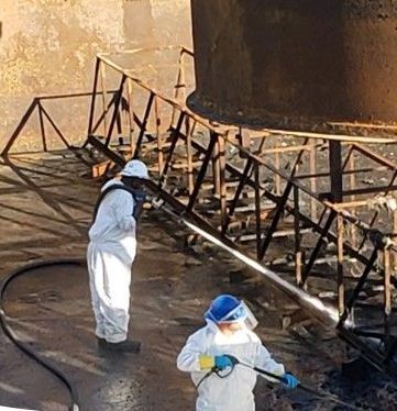 Two First environmental workers are cleaning a large tank with a hose.