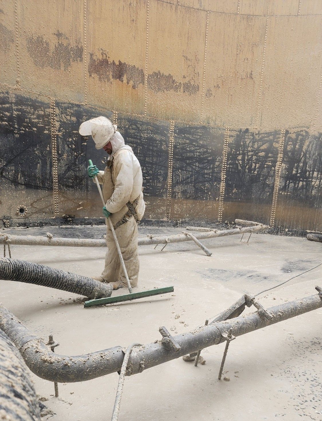 A man wearing a helmet and gloves is sweeping a concrete floor with a broom.