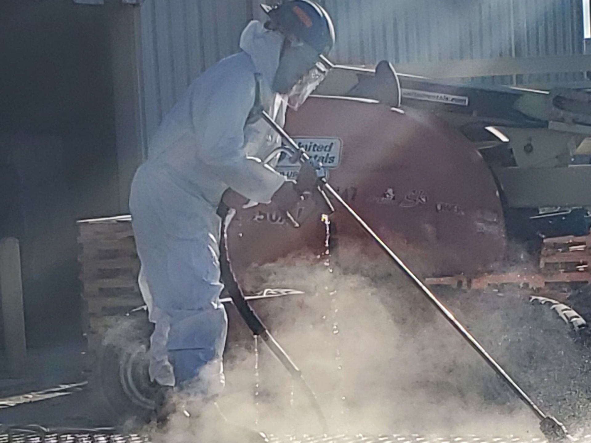 A First Environmental worker  in a protective suit is using an industrial pressure washer to clean factory