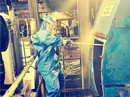 A First Environmental worker in a blue jumpsuit is cleaning a machine in a factory.