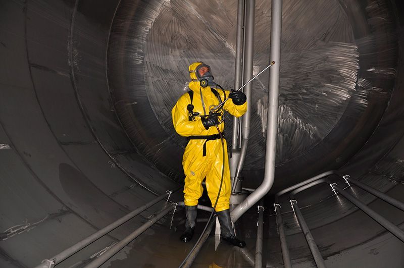 A man in a yellow protective suit is cleaning a large tank.