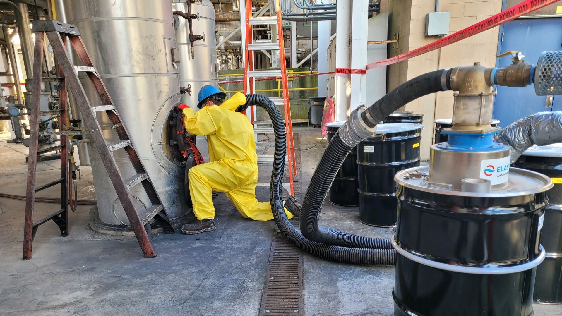 A First Environmental worker  in a yellow suit is working on a pipe in a factory.