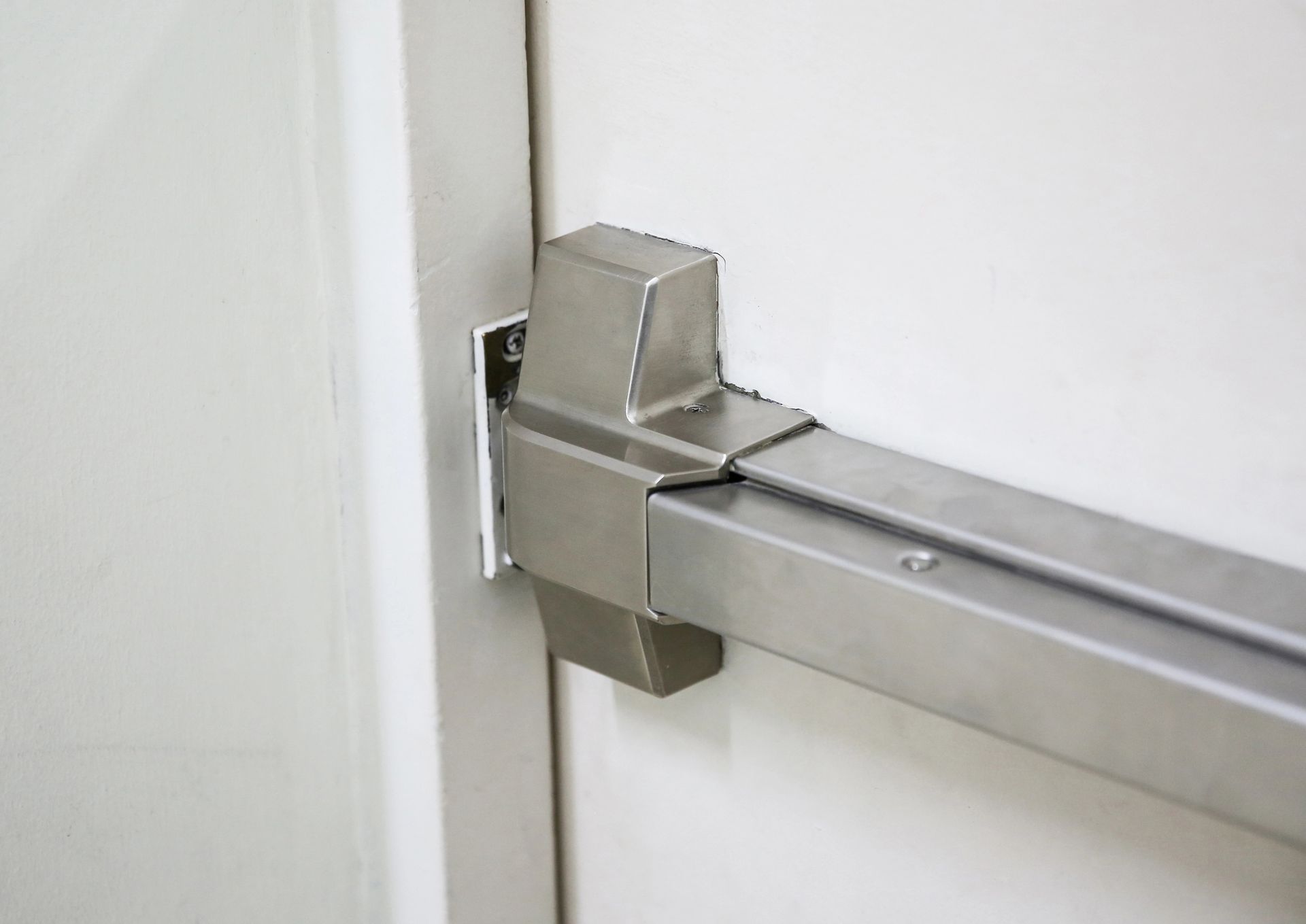Barra di spinta in metallo su uno stipite di porta bianco, probabilmente per un'uscita di emergenza.