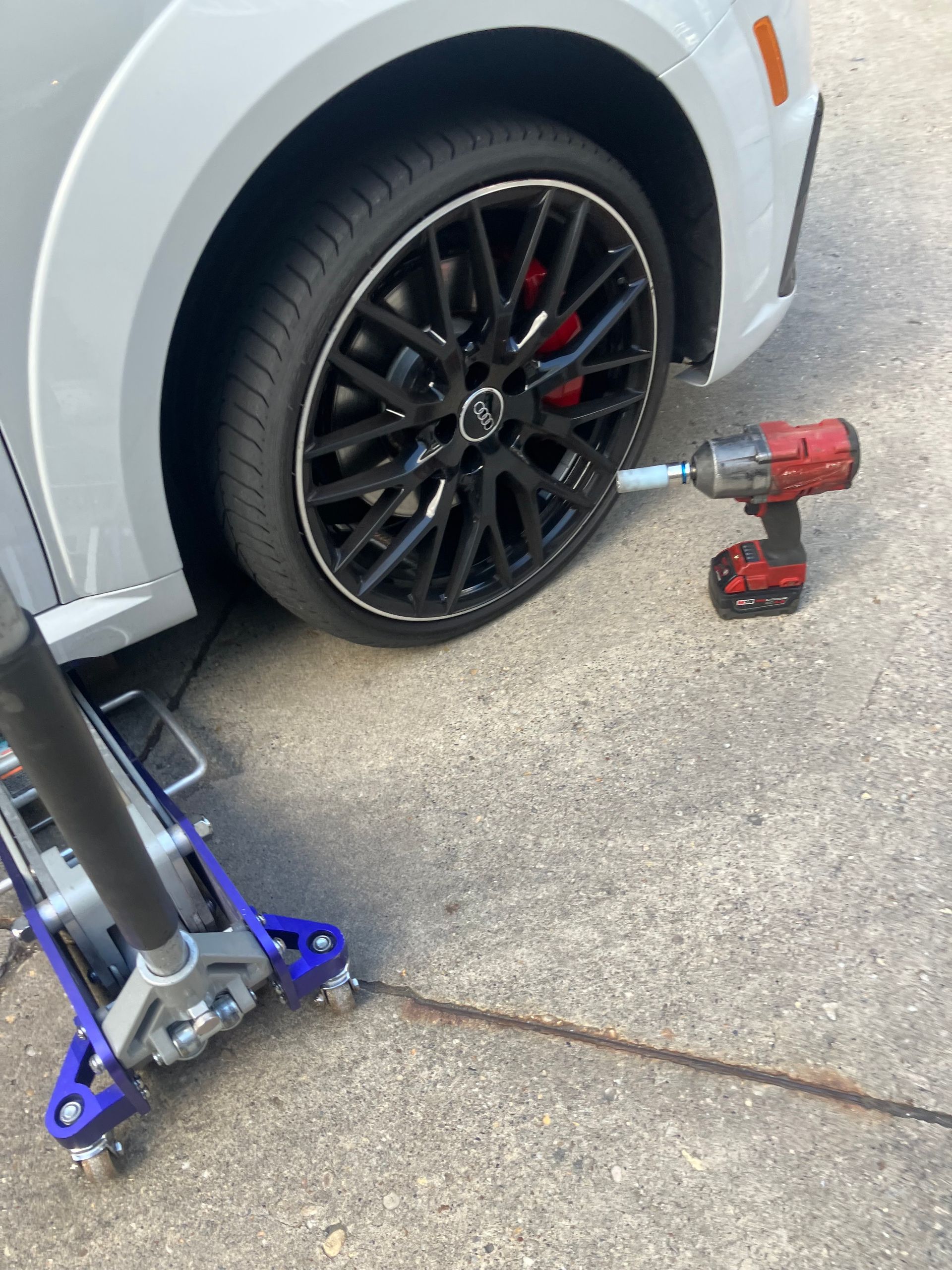 Car jacked up with wheel removed; cordless impact wrench and jack on driveway.