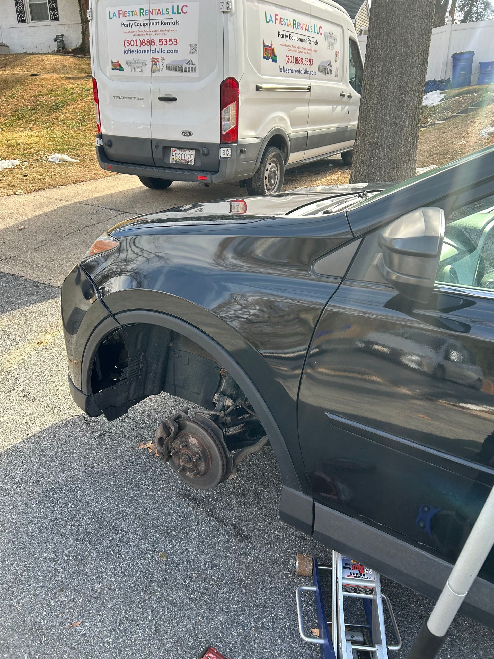 Black SUV with front wheel removed, parked on roadside next to a white van.