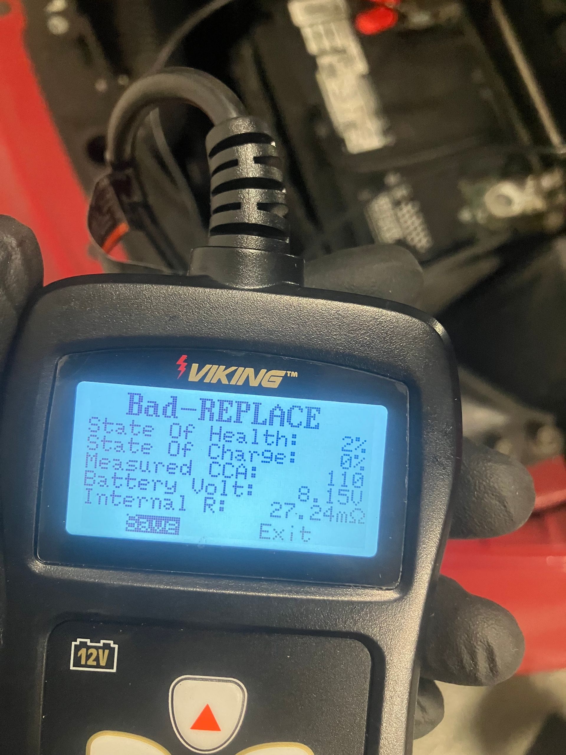 Close-up of a handheld diagnostic tool with a blue backlit screen reading “Bad REPLACE” in a workshop.