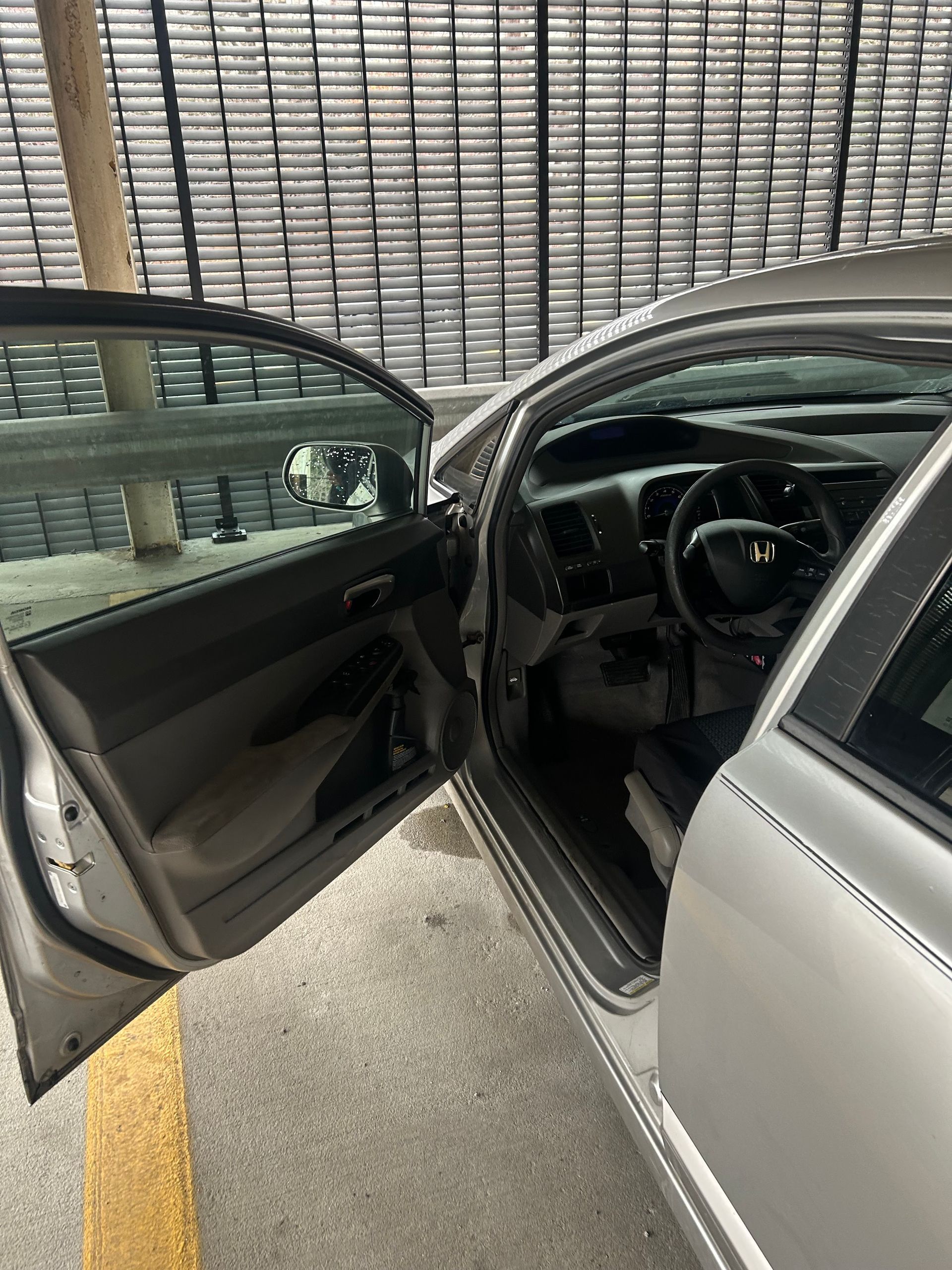 Open driver’s door of a silver car, showing the steering wheel and front seat inside.