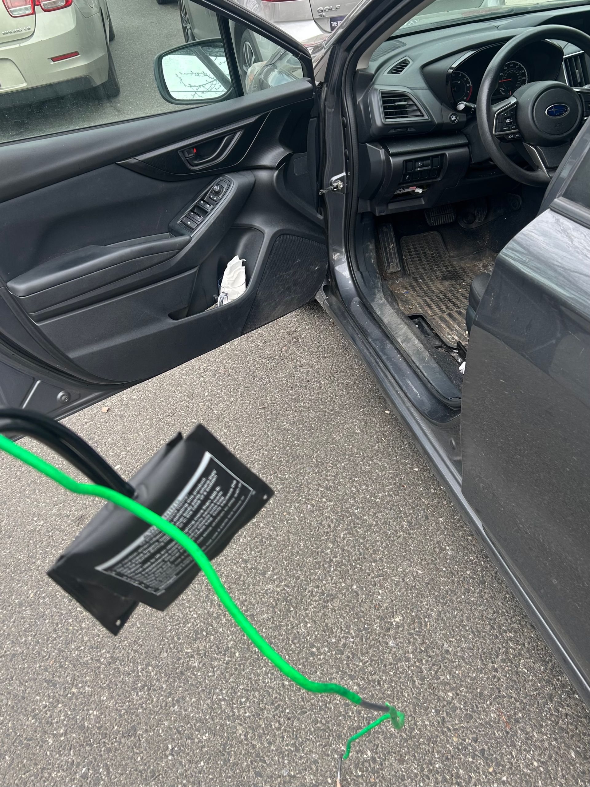 Open car door with black interior and a green cable lying on the pavement.