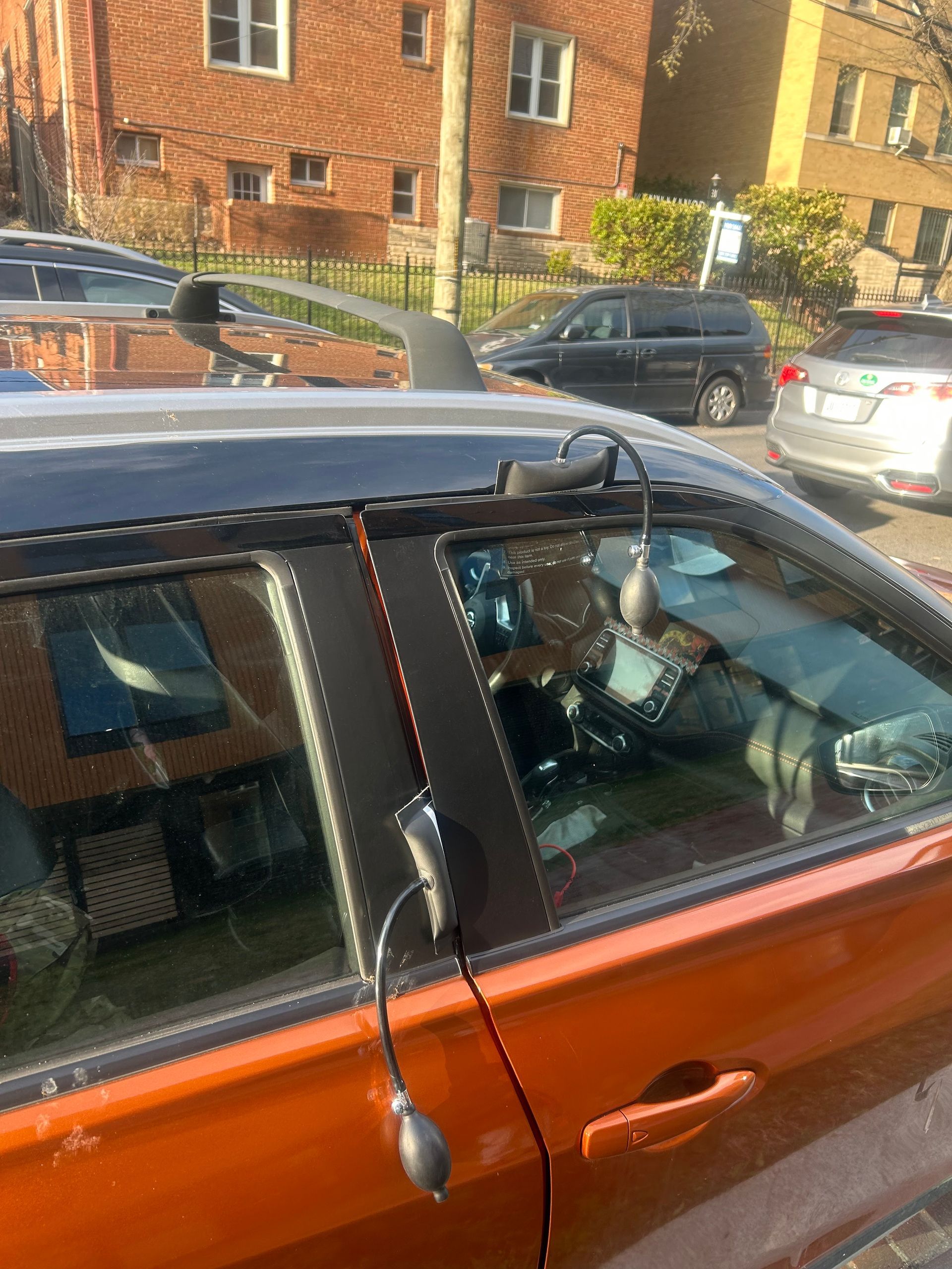Person in a black face mask sits in an orange car on a residential street.