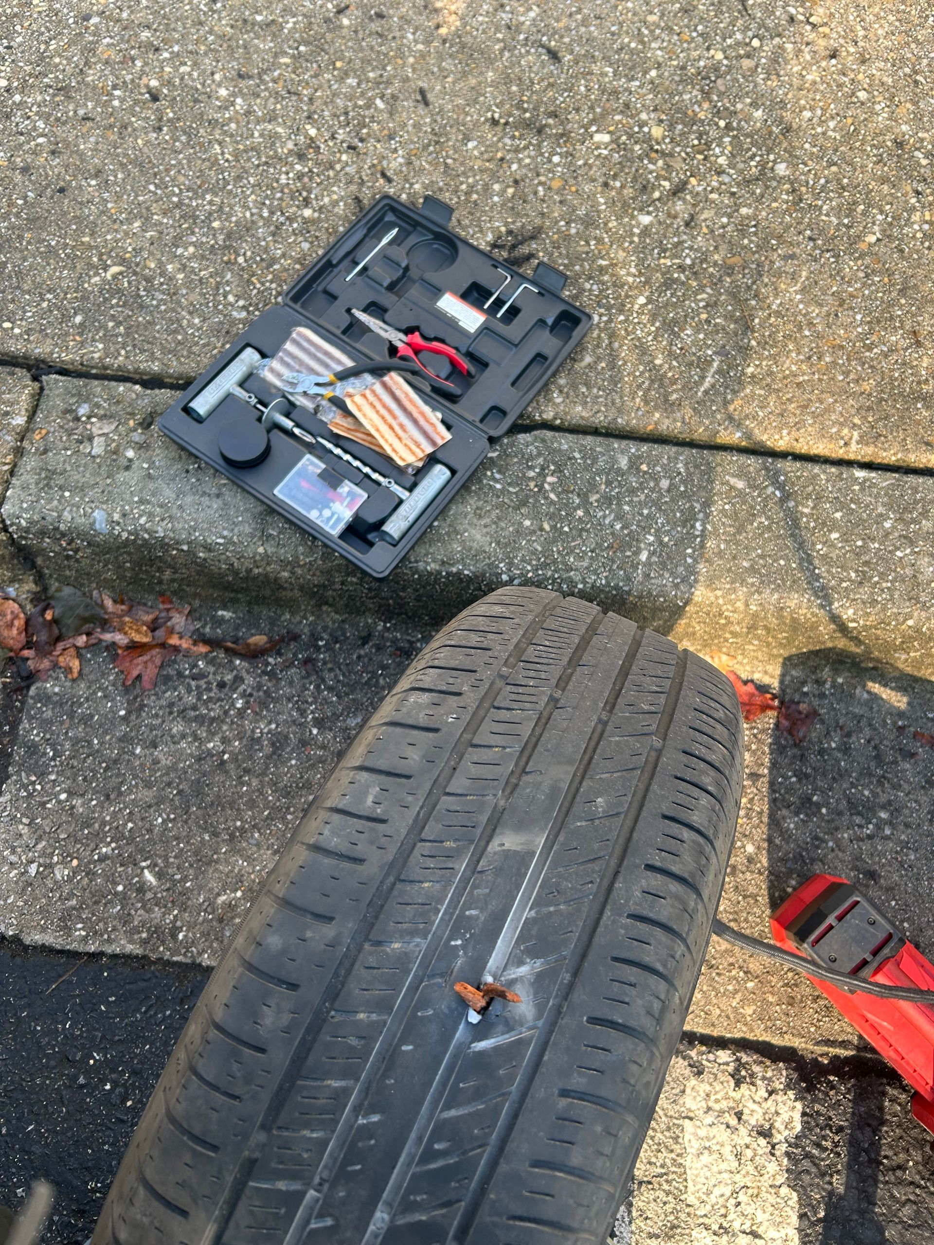 Car tire on curb beside an open tool case with tools on pavement