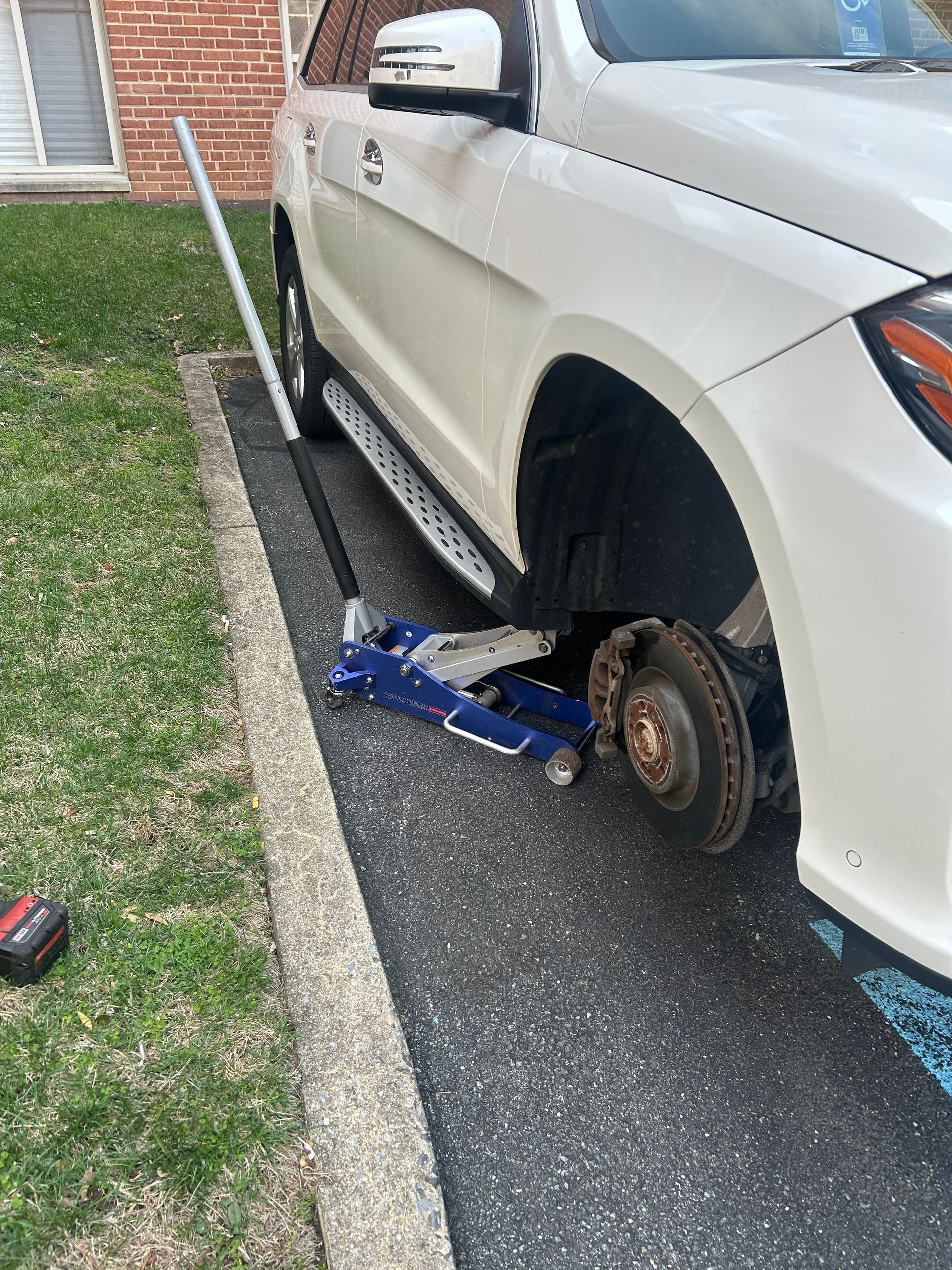 White SUV lifted on a blue jack with front wheel removed on a driveway near a brick house