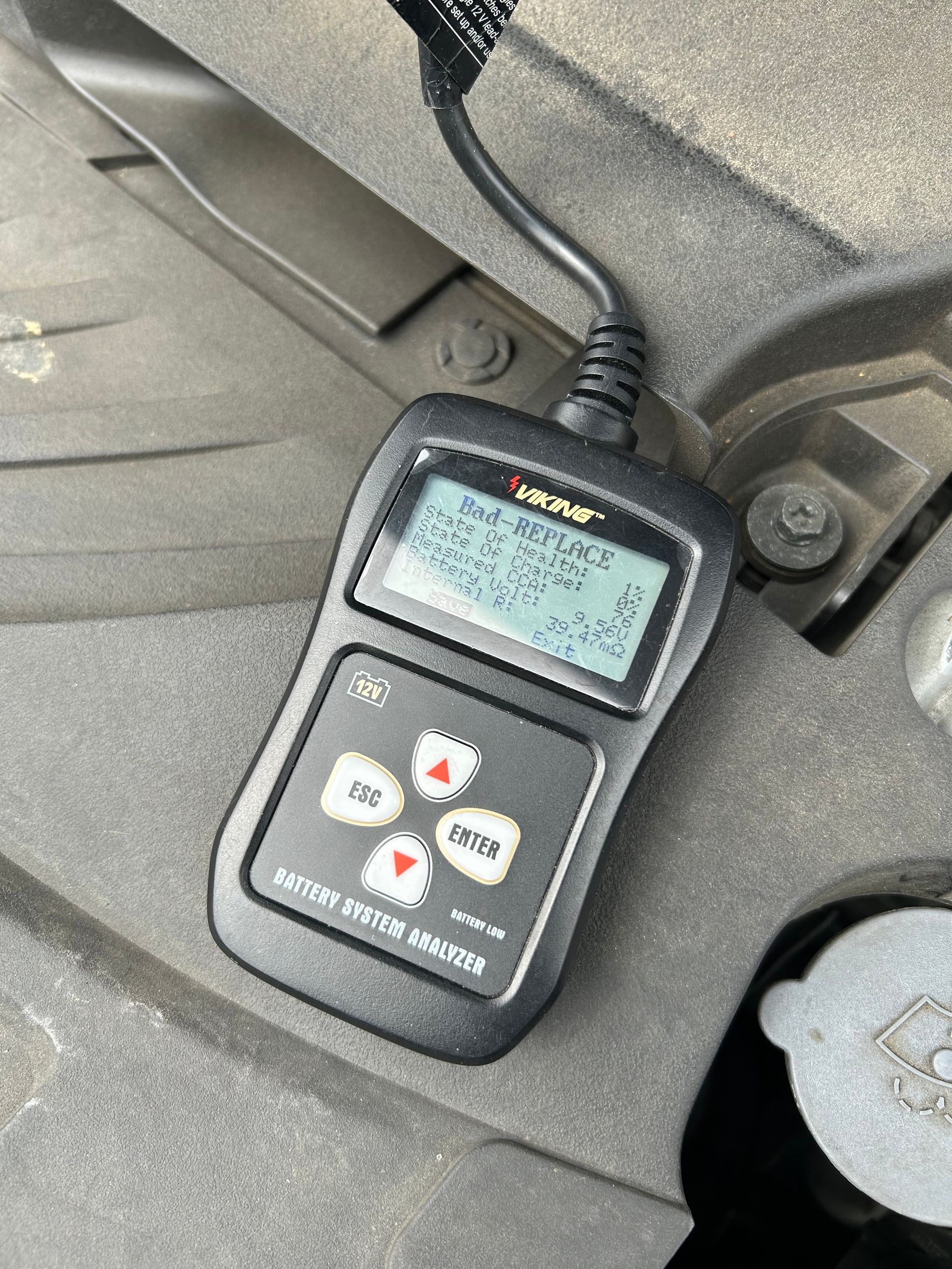Handheld car diagnostic scanner with display and buttons resting inside a vehicle.