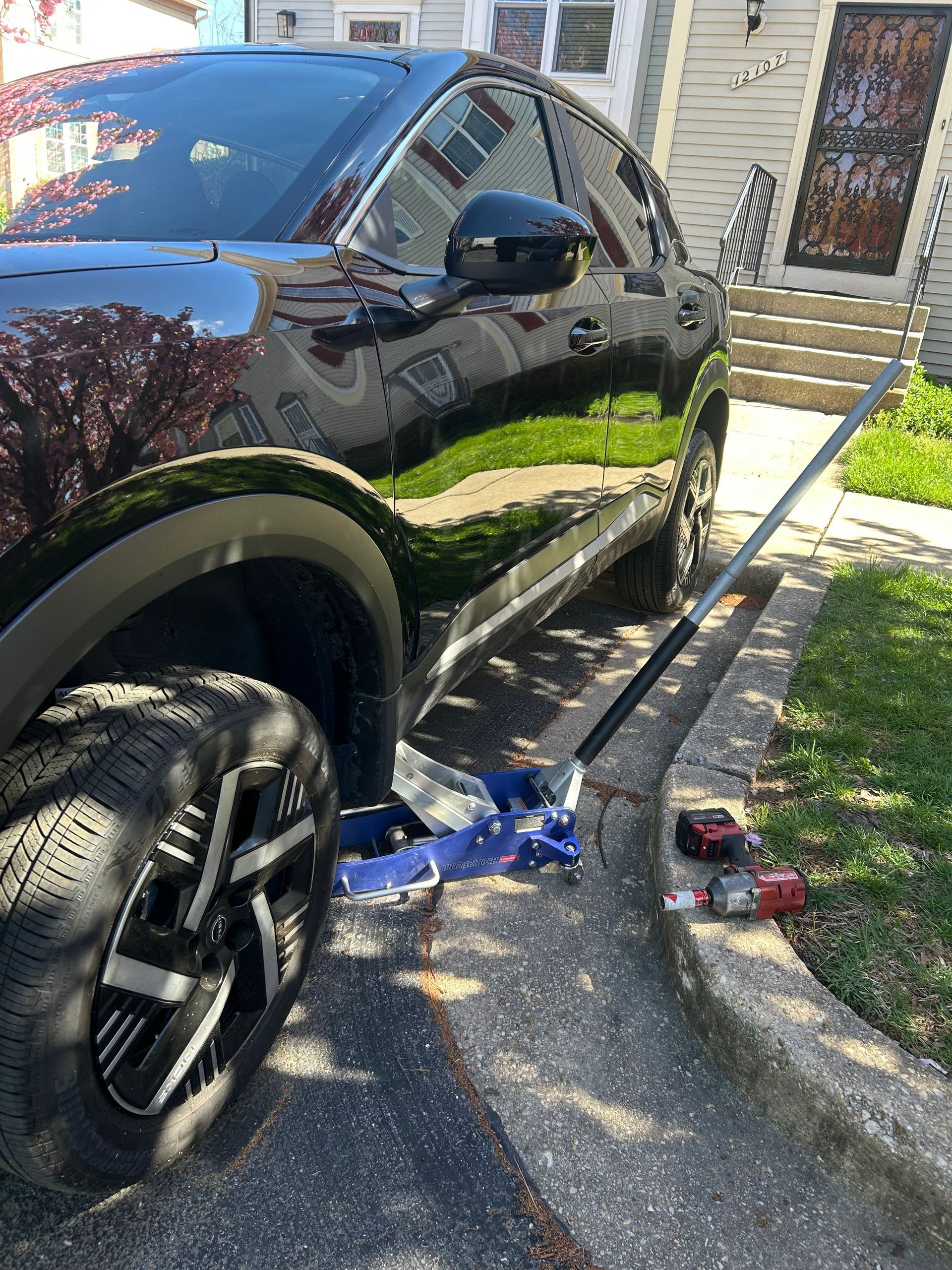 Black SUV parked in a driveway, with a flat front tire and debris scattered nearby.