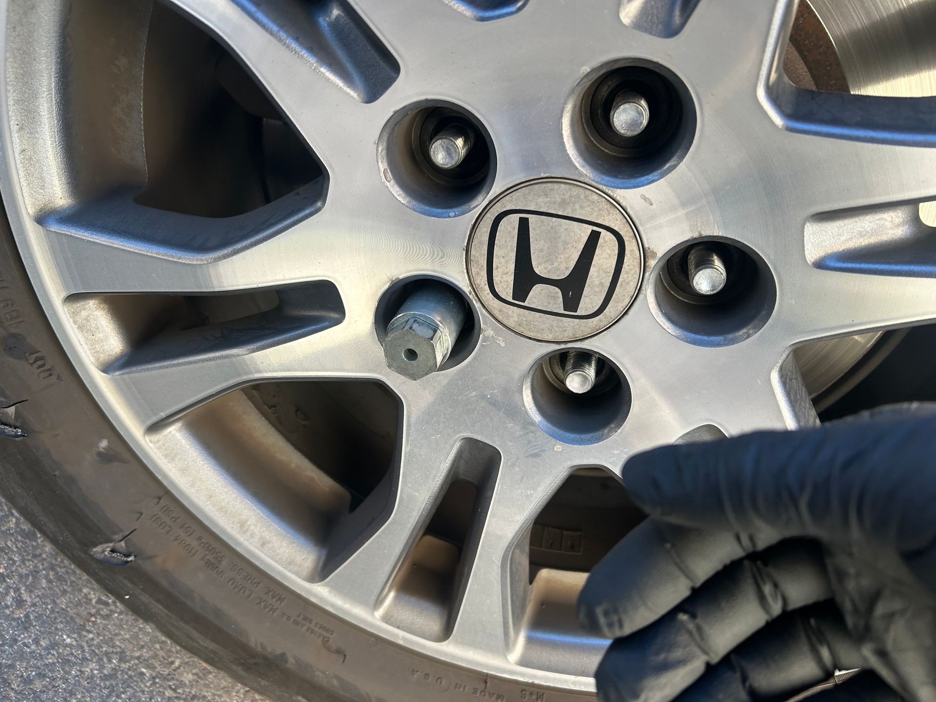 Gloved hand tightening a lug nut on a Honda car wheel rim