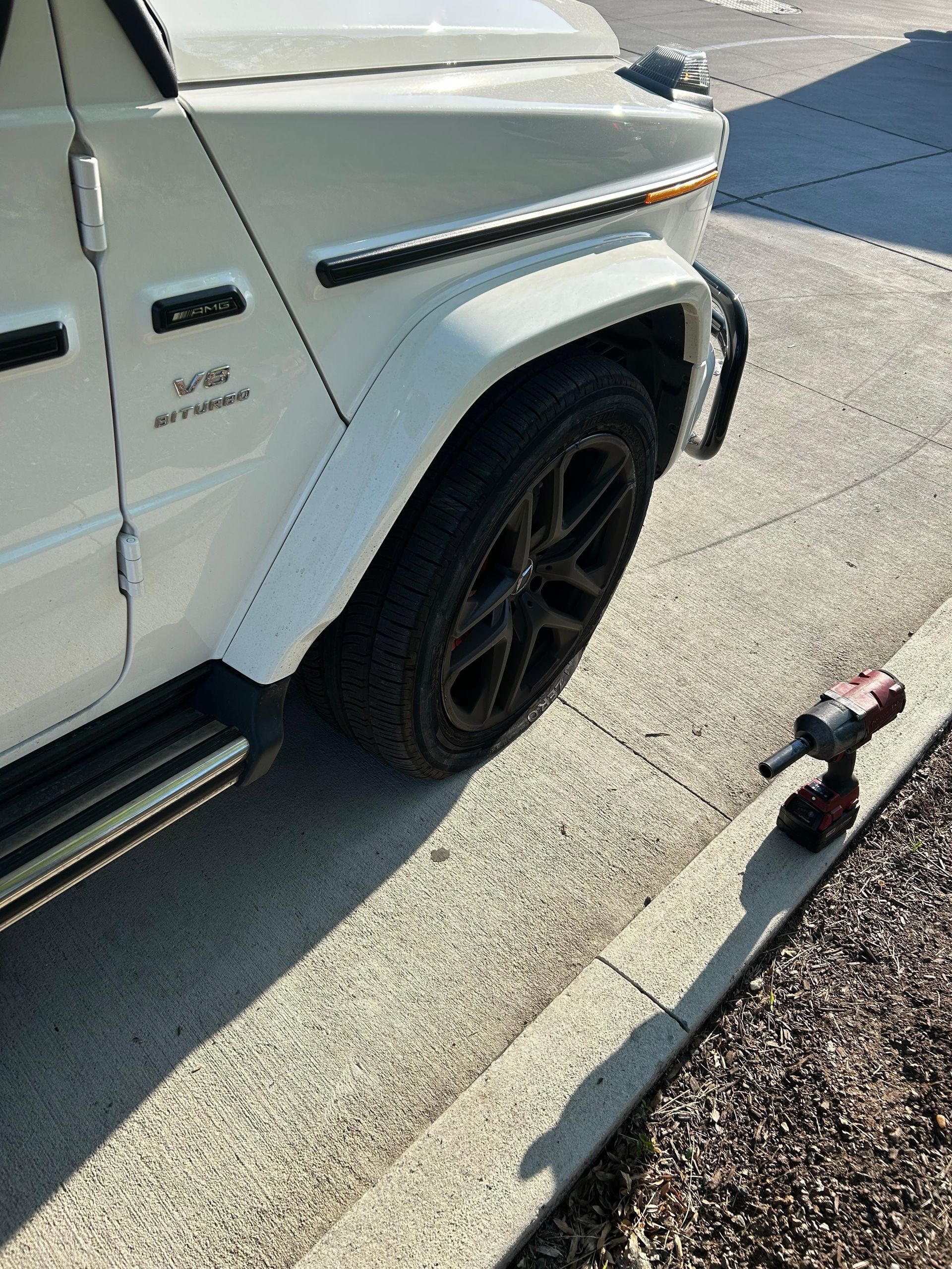 White SUV parked at curb with a power tool on the sidewalk beside the front wheel.