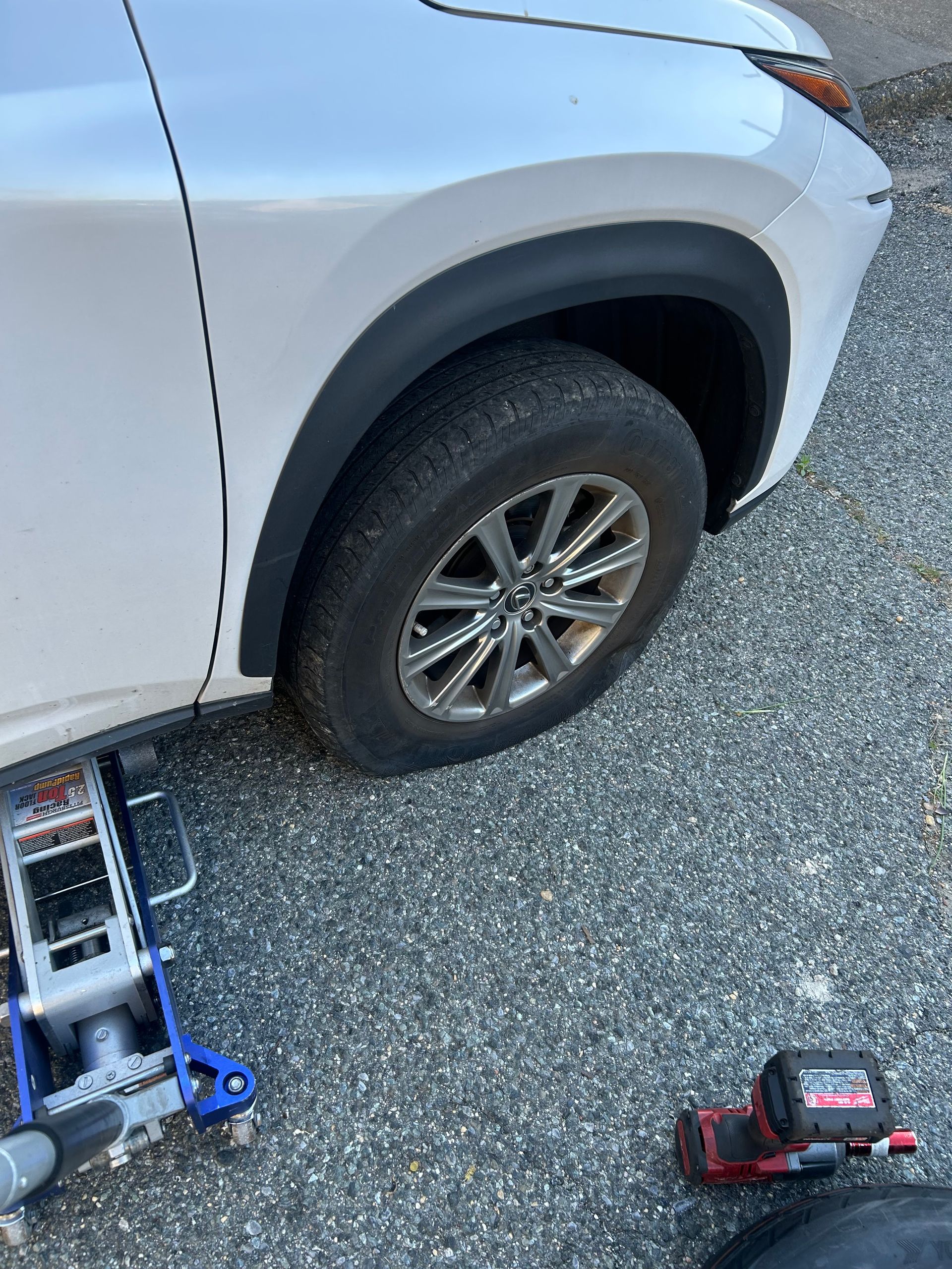 Silver SUV with a front wheel lifted, showing a blue jack and red power tool on the ground.
