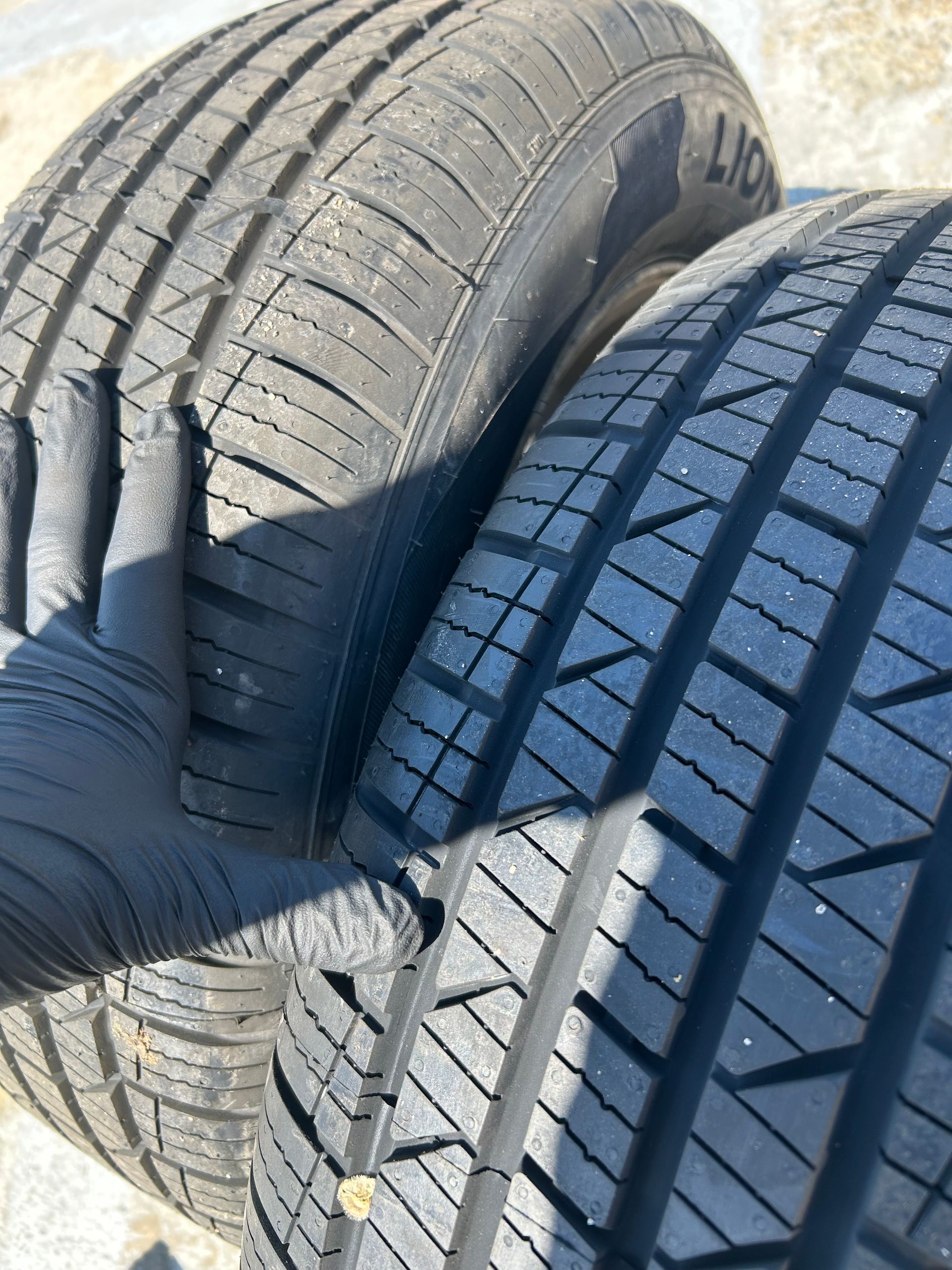 Gloved hand pressing two car tires side by side, showing tread patterns in bright sunlight