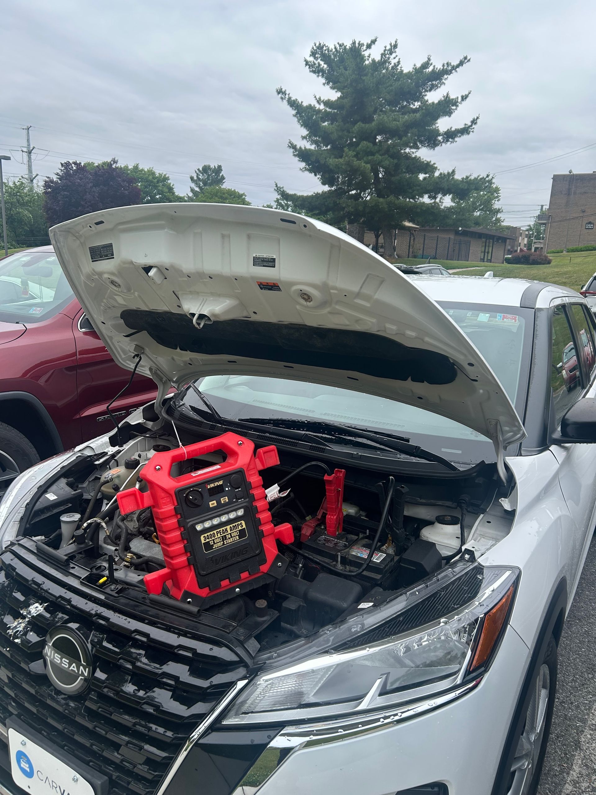 White sedan with hood open, showing a red backpack-style device in the engine bay, parked outdoors