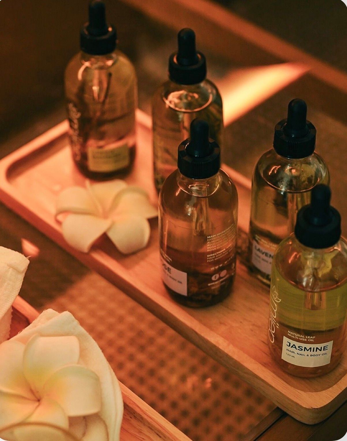 Glass dropper bottles of hair and scalp treatment oils arranged on a spa tray with white flowers