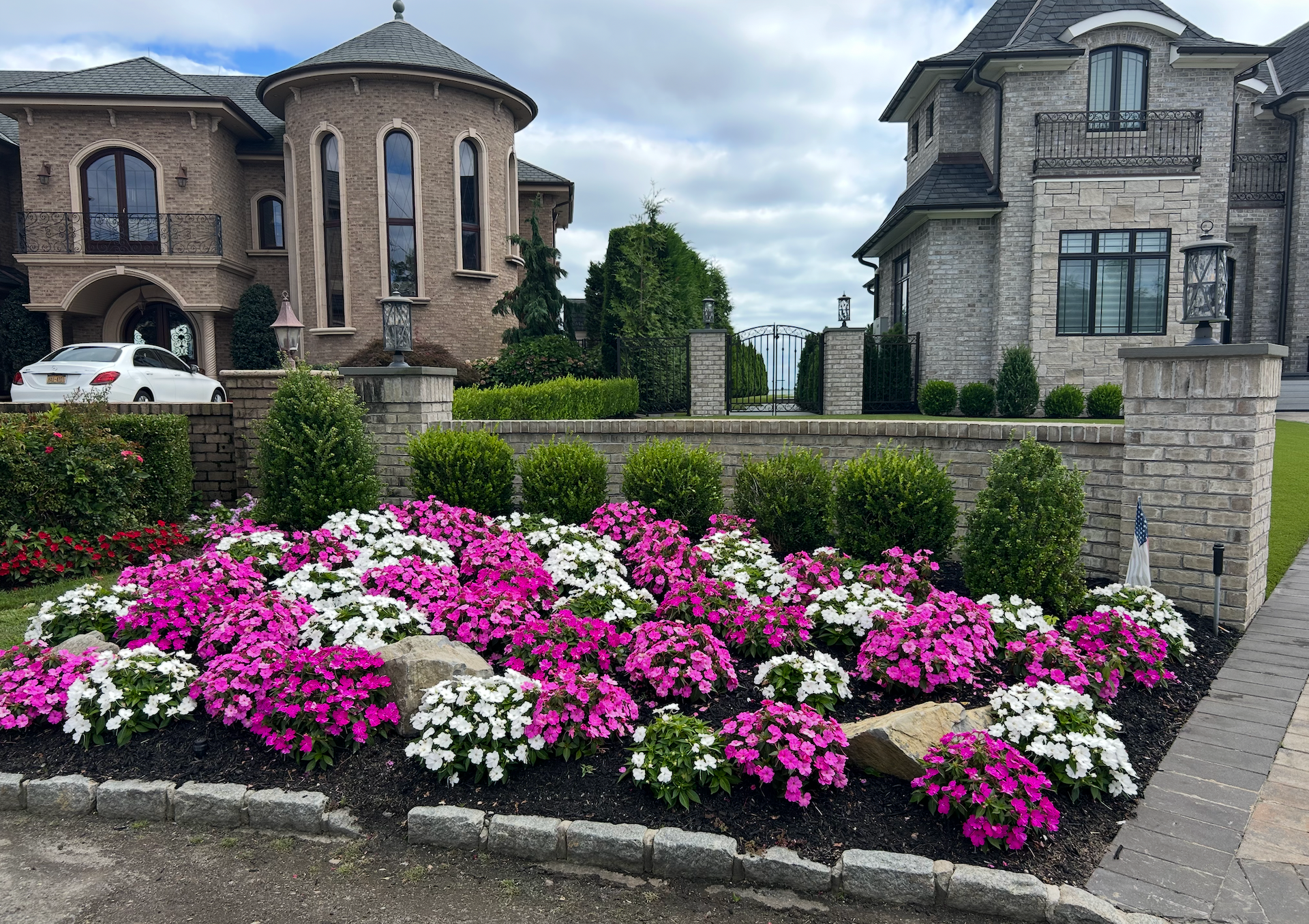 Two landscapers in neon vests trimming shrubs beside a house and driveway