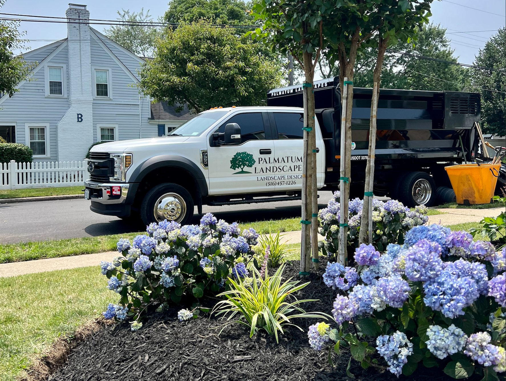 Gardener in green shirt walking along a stone path through a lush garden toward a house