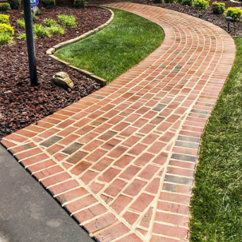 Curved brick garden pathway bordered by mulch, grass, and planting beds