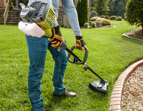 Person using a string trimmer to edge a green lawn beside a brick border