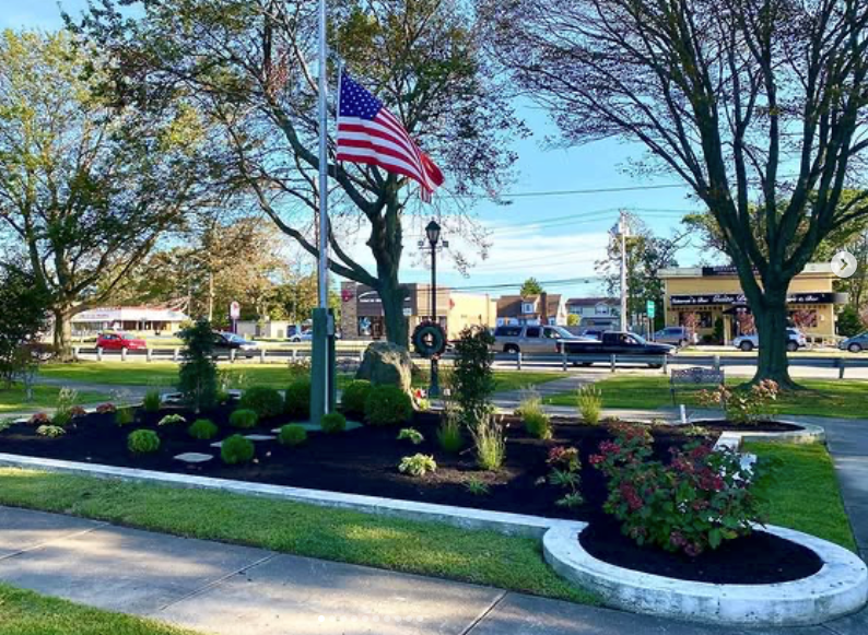 American flag in a landscaped park median with trees and flower beds on a sunny day