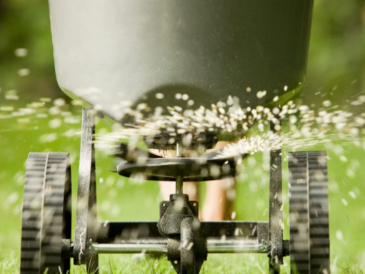 Close-up of a garden spreader scattering white granules over green grass