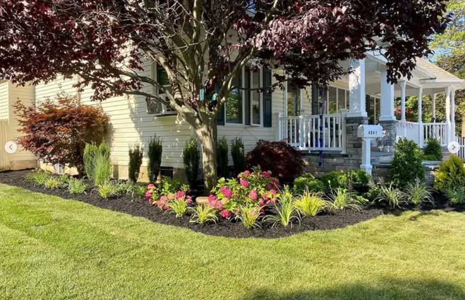 Front yard garden with colorful flowers, trimmed shrubs, and a porch beside a house