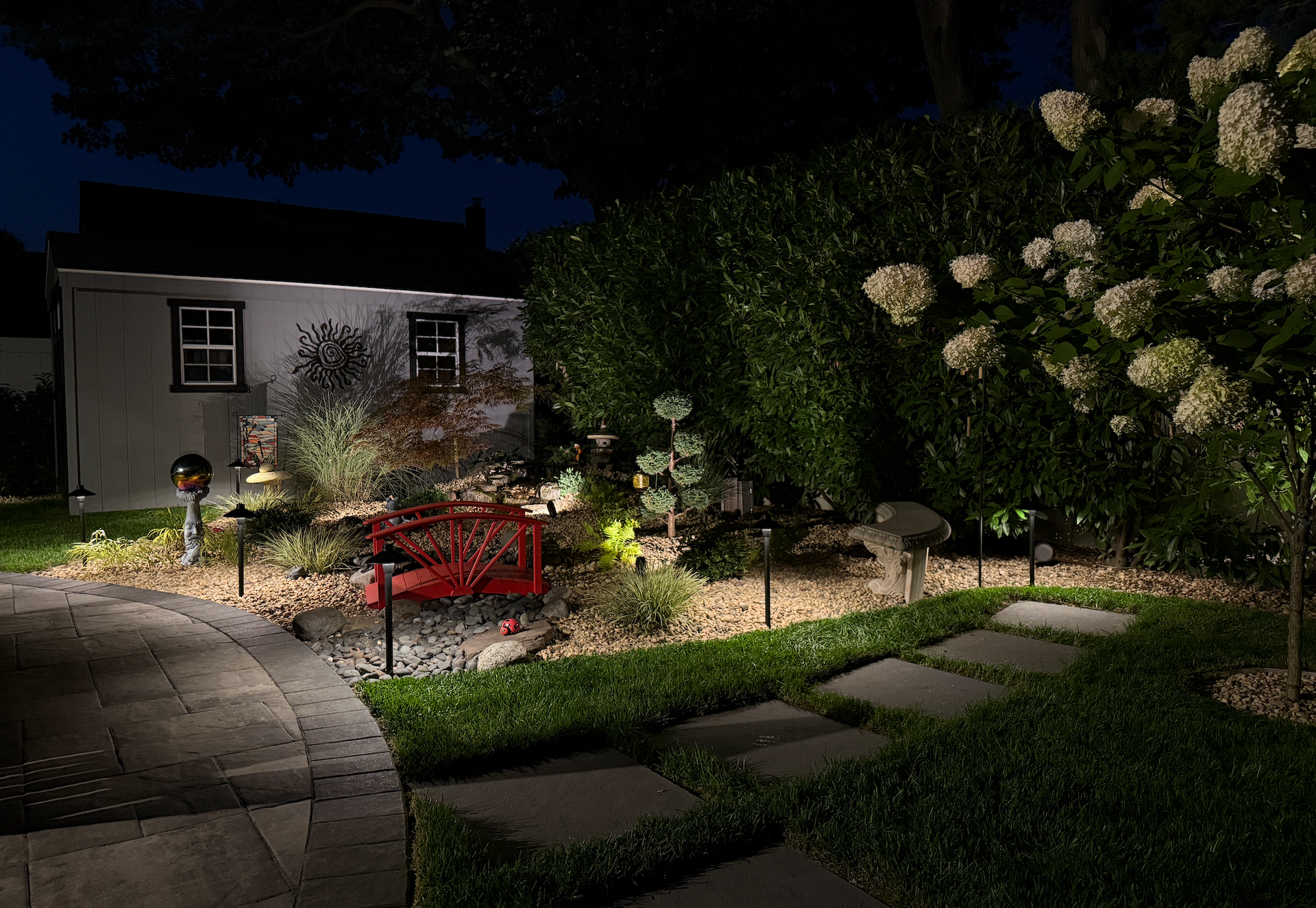 Illuminated garden tree at night with landscape lighting and a house in the background