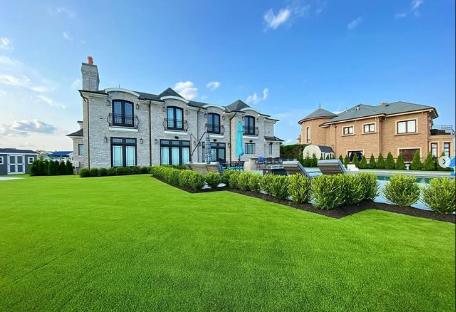 Large modern stone house with manicured green lawn and blue sky, viewed from the front yard