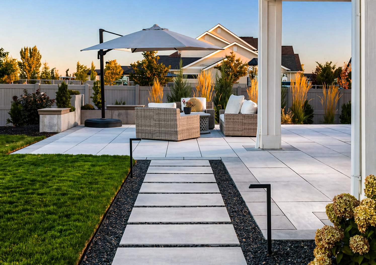 Modern patio garden with stone path, white pavers, umbrella, and outdoor seating at sunset