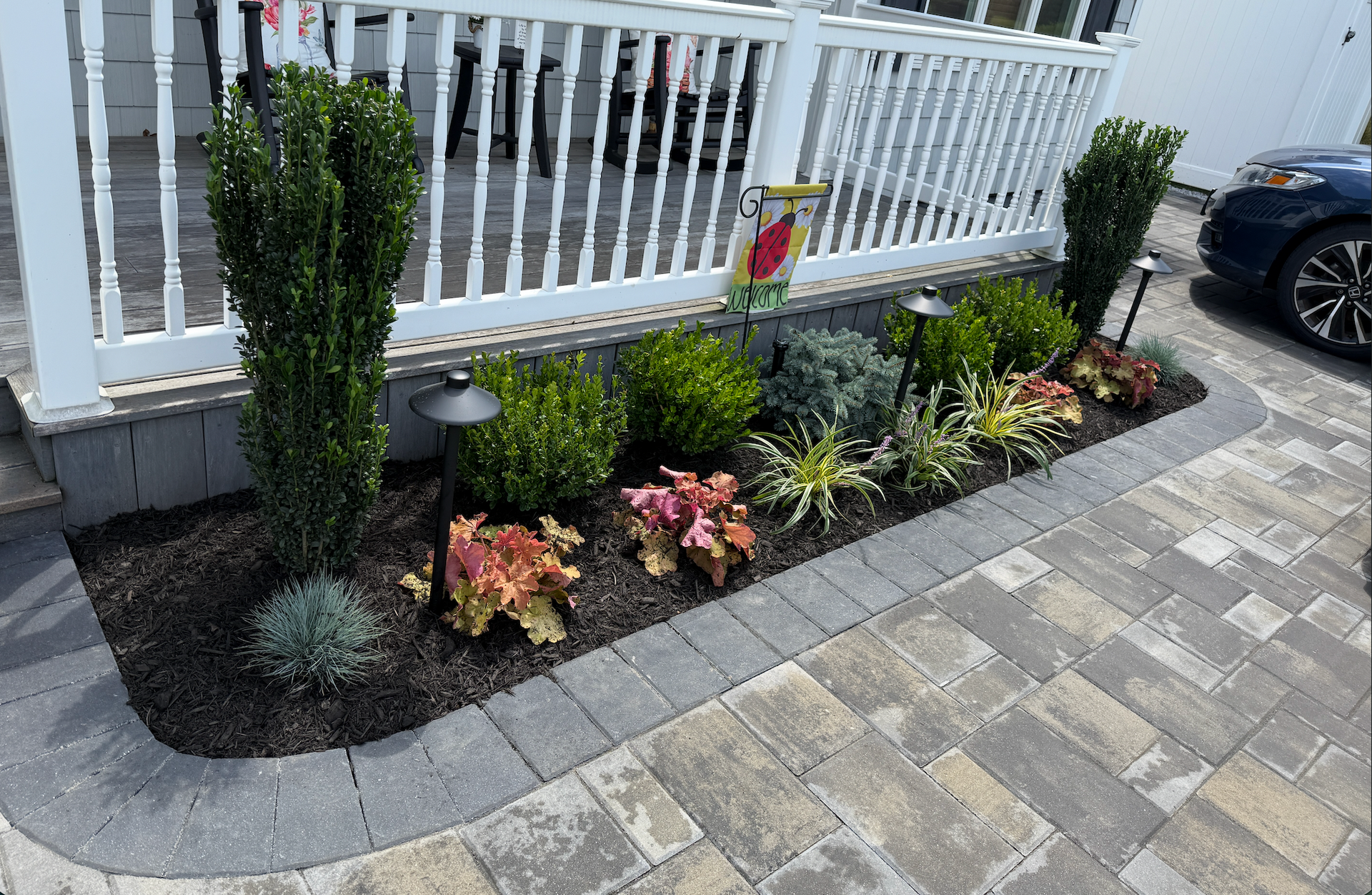 Stone patio with large gray pavers outside a building, with planters along the edge.