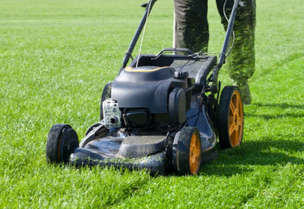 Black lawn mower with yellow wheels on a green grass lawn, being pushed by a person partly visible