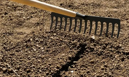 Garden rake dragging through dry soil, leaving a furrow on a dirt surface