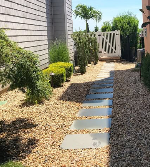 Stepping-stone path through a landscaped side yard to a white gate, with shrubs and gravel mulch