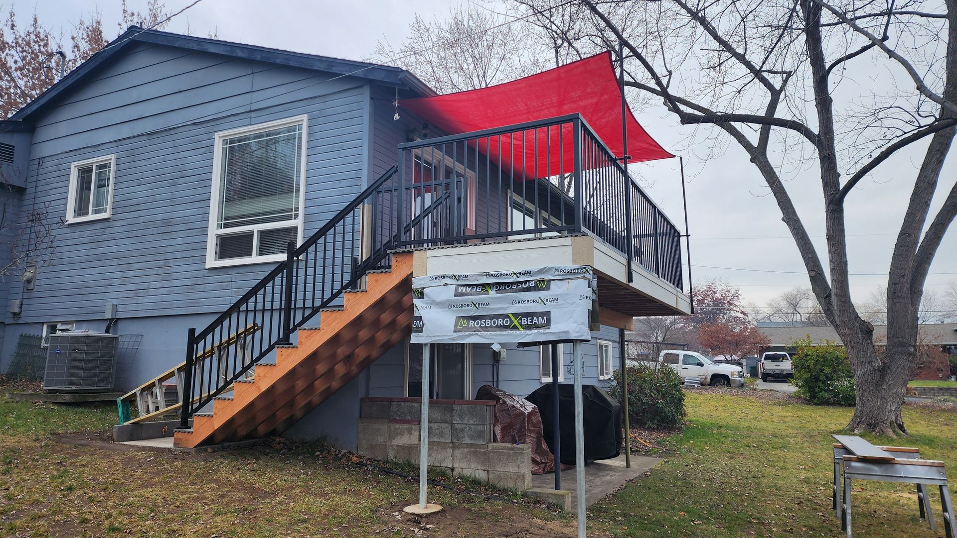 Blue house with a raised wooden deck, black railing, and red shade.