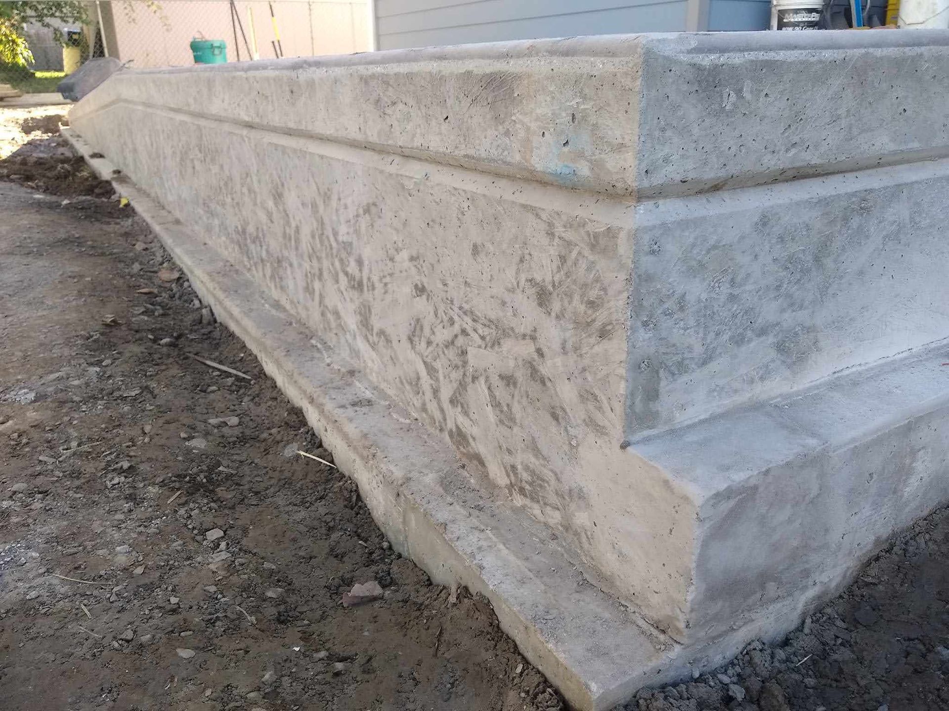 Concrete foundation corner; freshly poured, unfinished appearance, set in dirt.