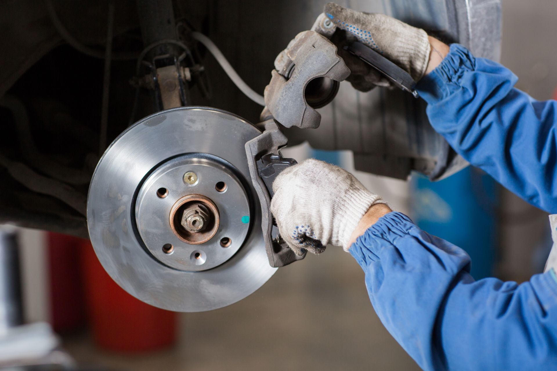 Mechanic in blue gloves tightening a car brake disc with a tool in a garage