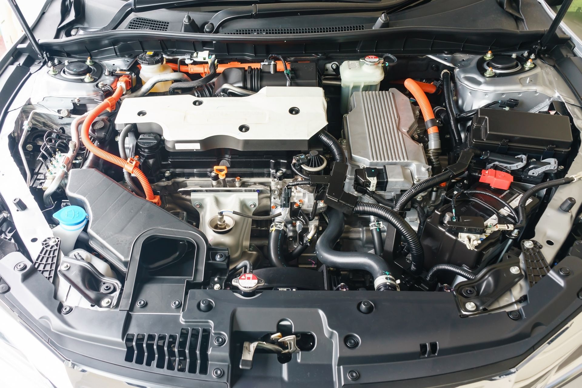 Car engine bay with orange high-voltage cables and a white engine cover, viewed from the front