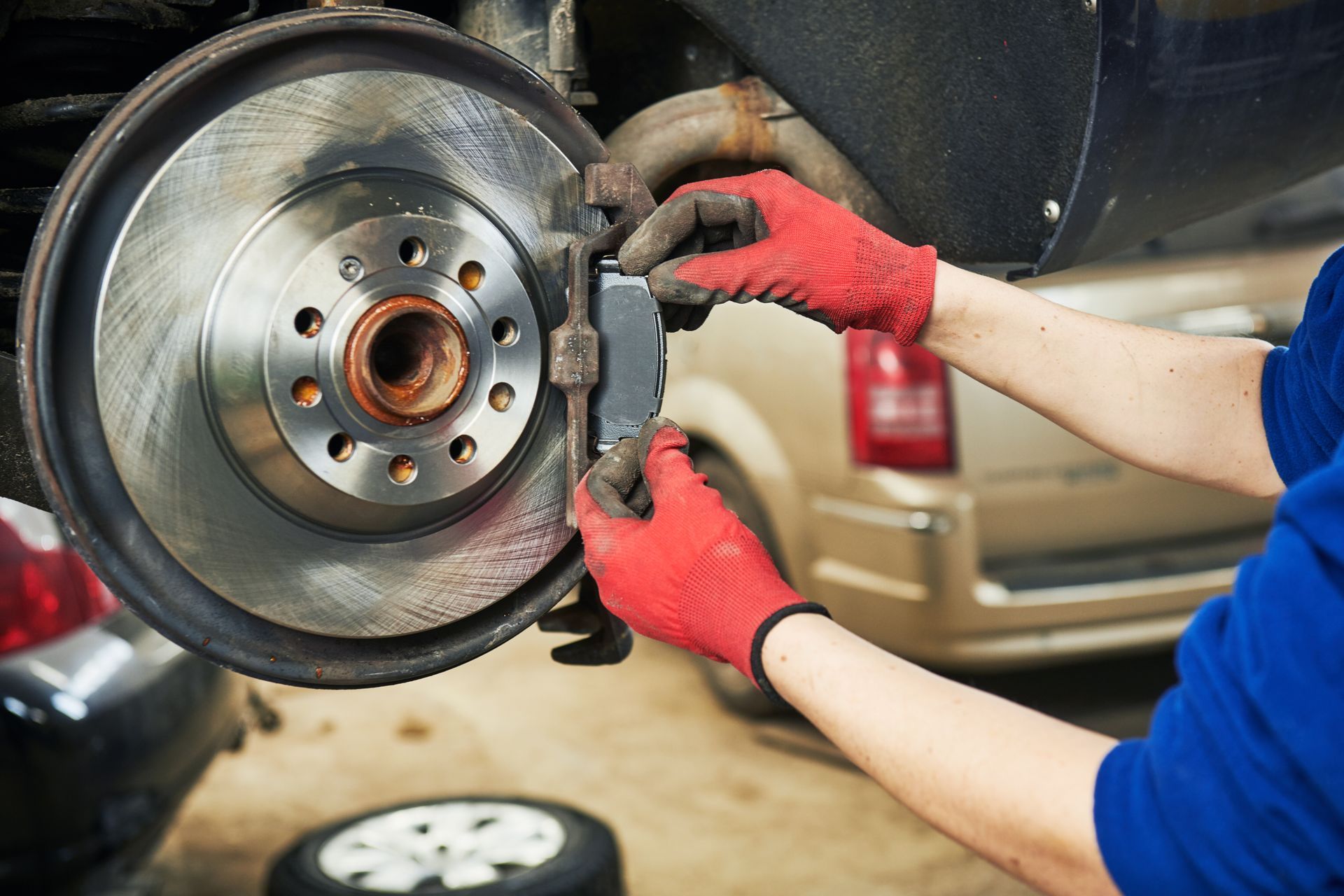 Mechanic in red gloves installing a brake rotor on a car wheel hub in a garage