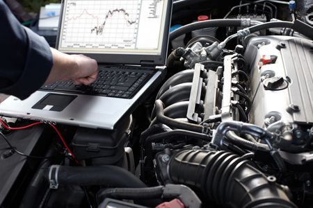 Mechanic using a laptop to diagnose a car engine in an open engine bay
